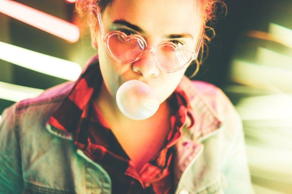 young girl blowing bubble gum and looking at the frame illuminated neon yellow light millennial woman t20 0XEy0B