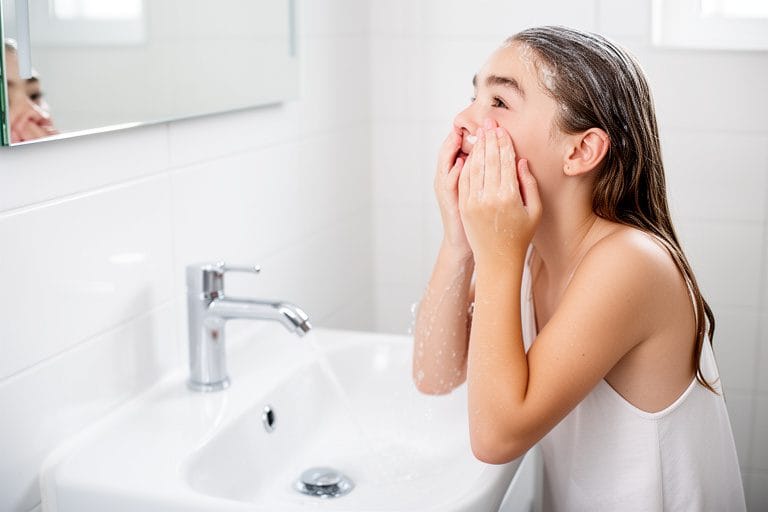 a photorealistc image of a teen washing her face in a clean, brighth bathroom sink area