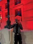 Darkson posing in front of a red-lit building at night