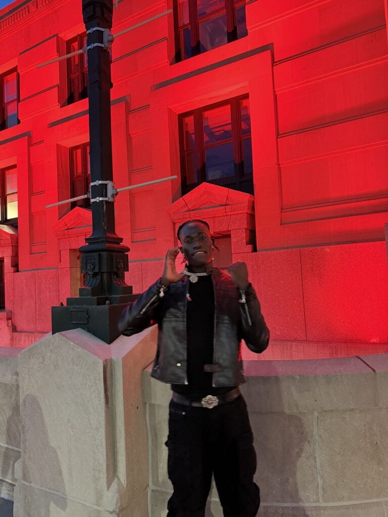 Darkson posing in front of a red-lit building at night